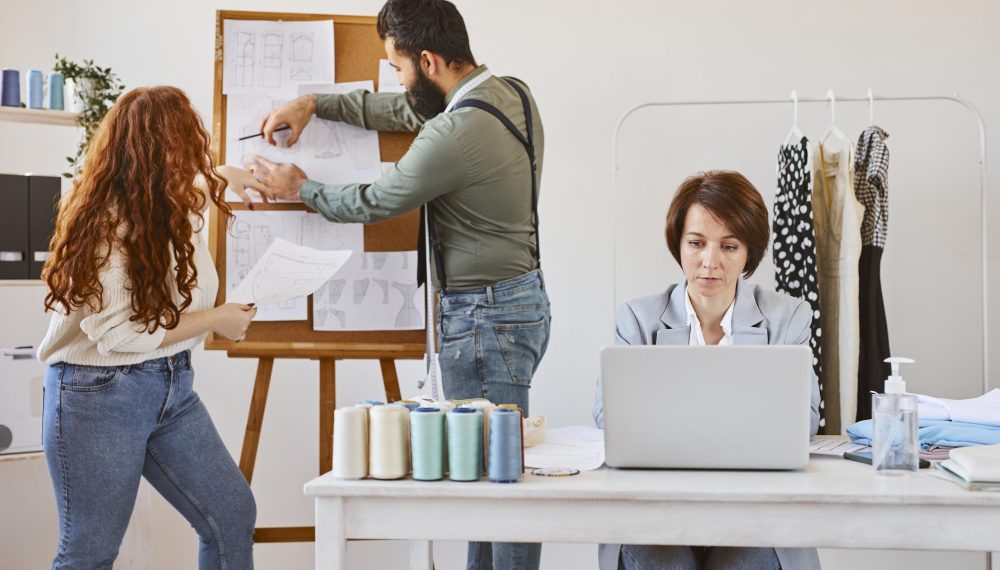 front-view-female-fashion-designer-working-atelier-with-laptop-colleagues